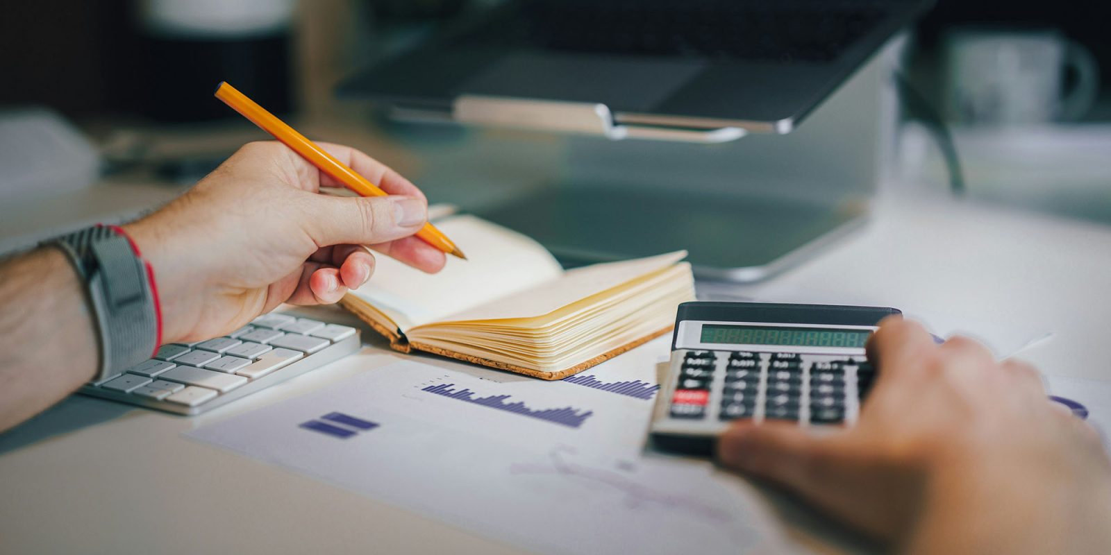 Legacy AT&T unlimited plans face price hikes, and it's a mess | Photo shows a man with a calculator, notebook and MacBook with graphs on the desk