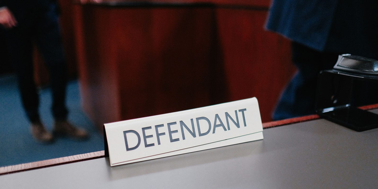 Apple faces yet another lawsuit over App Tracking Transparency | Photo shows a defendant nameplate in a courtroom