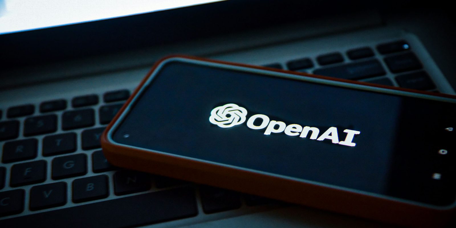 OpenAI calls trade secret dispute a mess of Apple's own making | Image shows an iPhone sitting on a MacBook keyboard with the OpenAI logo displayed
